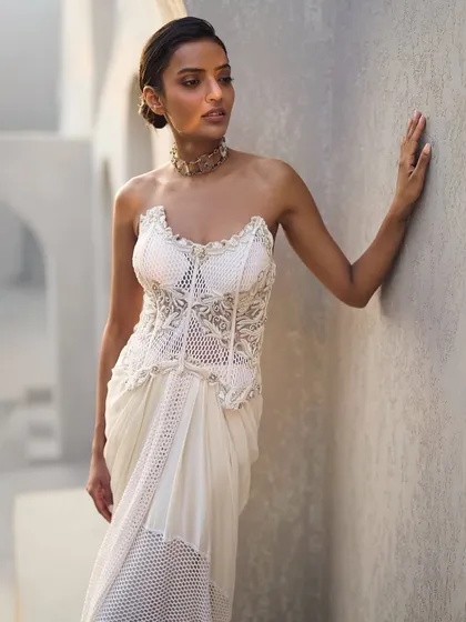 An ivory gown where sculpted sophistication meets artful drapes. This piece is adorned with delicate embellishments, with every detail telling a story of modern elegance.