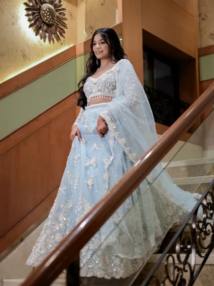 A full-length shot of the bride on a grand staircase, looking off to the side. The composition uses the elegant railing and stairs to frame her beautifully.