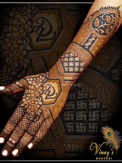A unique back-of-hand design featuring the couple's initials 'D' and 'G' in a floral crest on the palm. The arm is decorated with auspicious Swastika symbols and geometric patterns.