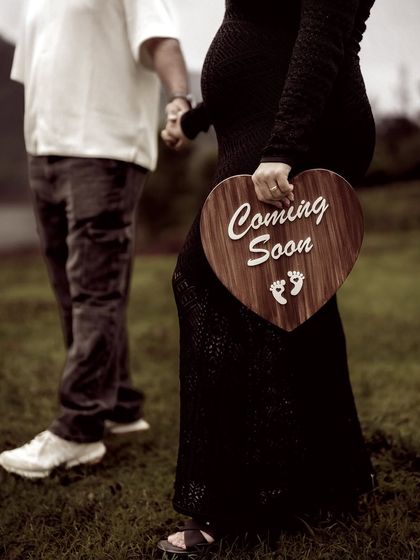 A detail-oriented shot of the couple walking, with the "Coming Soon" sign held between them. The focus on the sign and their connected hands tells a simple, sweet story.