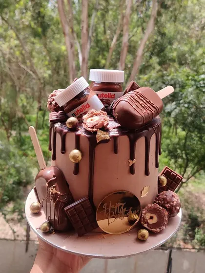 For the ultimate chocolate lover, I present the Nutella overload cake. This creation is dripping with rich chocolate ganache and loaded with Nutella jars, cakesicles, Ferrero Rocher, and chocolate bars for a truly decadent experience.