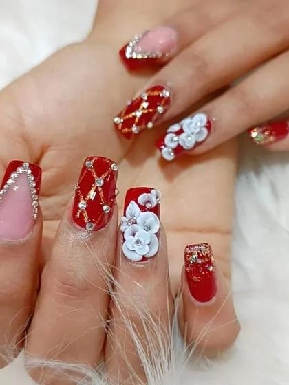 A close-up shot focusing on the detailed 3D floral work and crystal placement on this stunning red and pink bridal manicure.