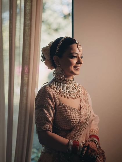 A beautiful bridal portrait by a window, the soft natural light highlighting her smile and the intricate details of her jewelry.