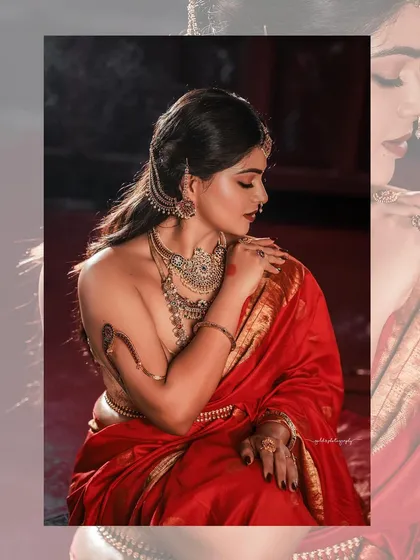 A modern take on a classic pose, this image emphasizes the beautiful lines of the backless blouse and the elegant drape of the red silk saree. The lighting is soft yet dramatic, highlighting the bride's profile and the antique jewelry.