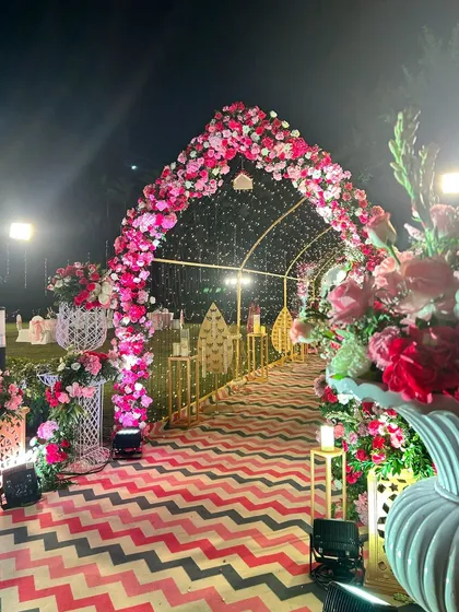 This grand floral archway, illuminated by a canopy of fairy lights, creates a magical and romantic entrance for an outdoor evening wedding.