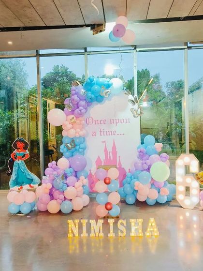 A dreamy 'Once upon a time' princess theme featuring cutouts of Princess Jasmine and Snow White. The pastel balloon arrangement in shades of blue, pink, and purple, along with a castle backdrop, creates a fairytale setting.