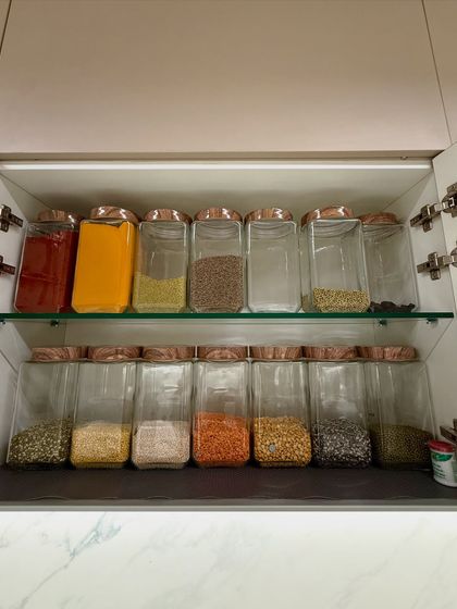 A two-tiered cabinet system with spices and dals stored in matching glass jars with copper lids. This setup is not only functional but also adds a touch of elegance to the kitchen decor.