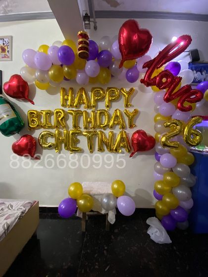 I can create custom birthday walls with the person's name and age, like this 'Happy Birthday Chetna 26' setup. The balloon arch uses a fun color combination of purple, yellow, and white, along with themed foils like a champagne bottle.