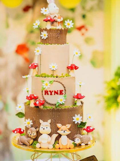 A magnificent four-tiered woodland cake for Ryne's birthday. The cake is decorated with a wood bark texture, edible mushrooms, daisies, and adorable fondant animals like a fox, squirrel, and hedgehog.