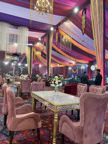 An elegant dining setup with dusty rose chairs and a mirrored table, set against a backdrop of purple and gold draping.