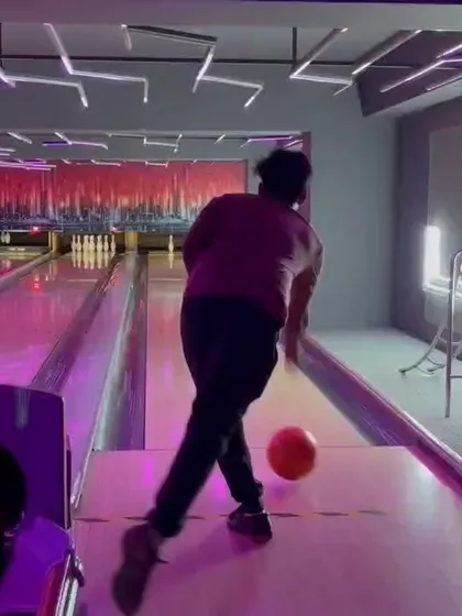 A dynamic shot of a player releasing the ball with a spin, under the pink and purple lights of our bowling alley.