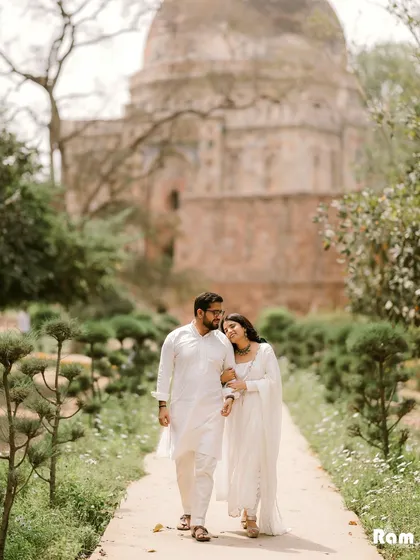 A classic walking shot through the lush gardens of Lodhi Garden in Delhi, with a historic tomb in the background. This image captures a relaxed, romantic stroll, blending nature and history.
