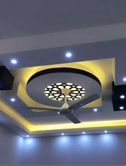 A modern bedroom ceiling that incorporates a fan and a backlit 'jaali' or lattice panel. This design is both functional and highly decorative.