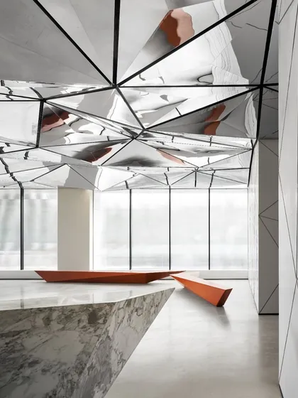 The lobby's design balances bold geometry with warm accents. The reflective ceiling and angular furniture are softened by natural light and the rich color of the seating.