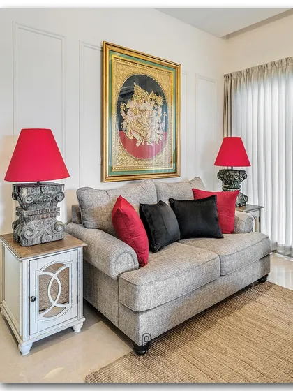 A cozy seating area where traditional art meets bold color. A classic Ganesha painting is flanked by two vibrant red lamps, creating a symmetrical and visually powerful composition that feels both traditional and modern.