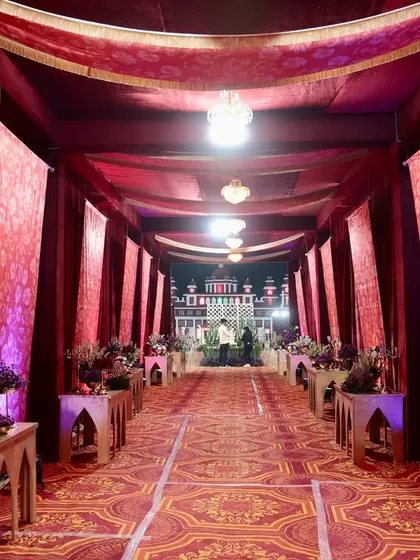 The main walkway for the event, lined with elegant consoles and draped in rich red fabrics, leading guests towards the grand palace structure.