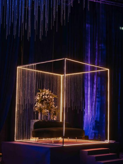 Another angle of the neon cube photo booth, showing how it stands out against the dark, draped background. The combination of sharp, modern lines and delicate, shimmering crystals makes for a visually striking installation.