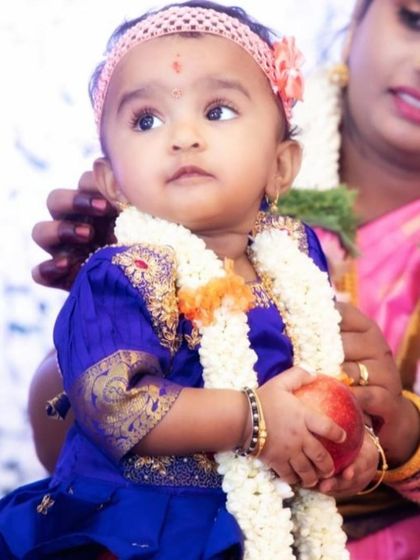 The same little princess in a traditional blue silk frock, adorned with a flower garland, looking up with curiosity.