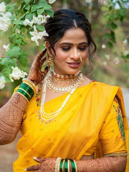 A vision of tradition and grace in a radiant yellow saree. The makeup is soft and glowing, with a focus on her eyes and the beautiful pearl-and-gold jewellery.