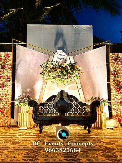 A stylish Mehendi stage for an evening event, featuring two beautiful flower walls illuminated by warm spotlights. The modern geometric backdrop adds a contemporary touch to the design.