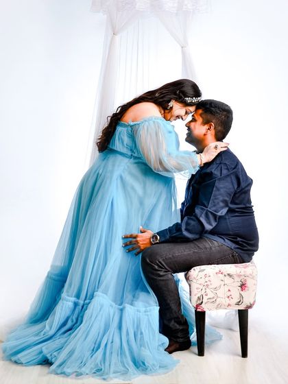 An intimate moment between an expecting couple during their maternity session. The mother-to-be's flowing blue dress and the soft white background create a bright and airy feel.