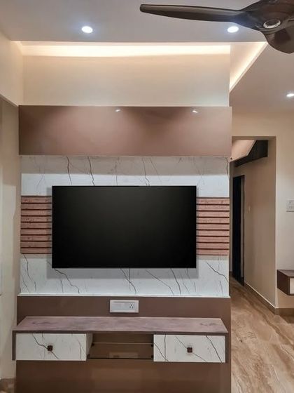 The TV unit in this project combines different textures, including wood grain, marble finish, and fluted panels, to create a visually interesting focal point.