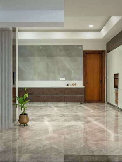 A spacious and elegant kitchen area defined by its clean lines and subtle textures. Grey marble-look flooring and wall panels are complemented by warm wood doors and minimalist cabinetry.