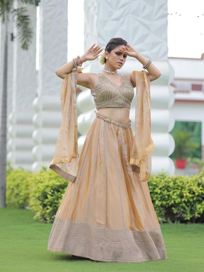 A dramatic pose in the gold lehenga, with the model's arms raised to show the flow of the dupatta.