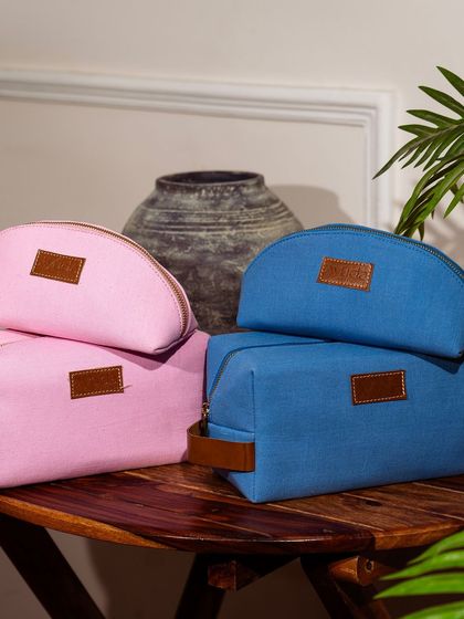 A collection of pink and blue toiletry bags styled on a wooden table with a rustic pot in the background, creating a warm, homey feel.