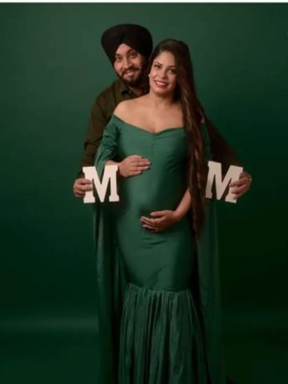 A couple's portrait featuring the bottle green mermaid gown. The "MOM" letters add a sweet, personal touch to this classic studio maternity photo.