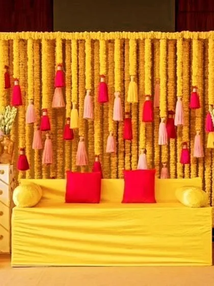 A simple and traditional Haldi backdrop made entirely of marigold flower strings. The colorful tassels add a playful element, perfectly complementing the bright yellow seating.