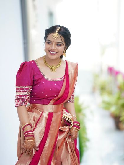 A smiling bride in her beautiful pink half-saree. Her makeup is fresh and glowing, perfect for a pre-wedding event.
