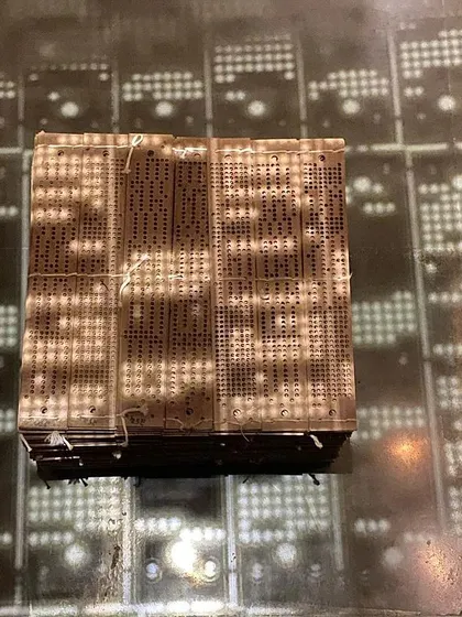 A close-up of a jacquard punch card installation, with its shadow projected onto the floor.