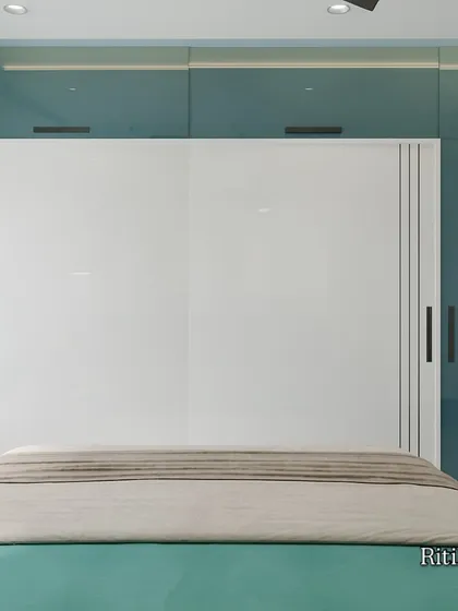This view focuses on the custom wardrobe solution in the teal bedroom. The combination of glossy white sliding doors and teal-colored panels creates a clean, contemporary look while offering efficient, space-saving storage.