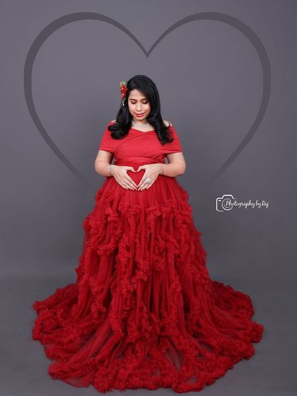 A beautiful studio portrait in a red ruffled gown. The heart-shaped hand gesture on the baby bump adds a sweet, symbolic touch.