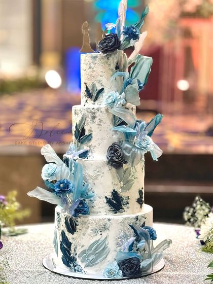This four-tiered wedding cake is a modern masterpiece. It features a silver leaf finish with abstract blue brushstrokes and is adorned with handmade sugar flowers and rice paper sails.