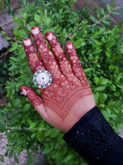 The large statement ring complements the intricate floral patterns on the fingers.