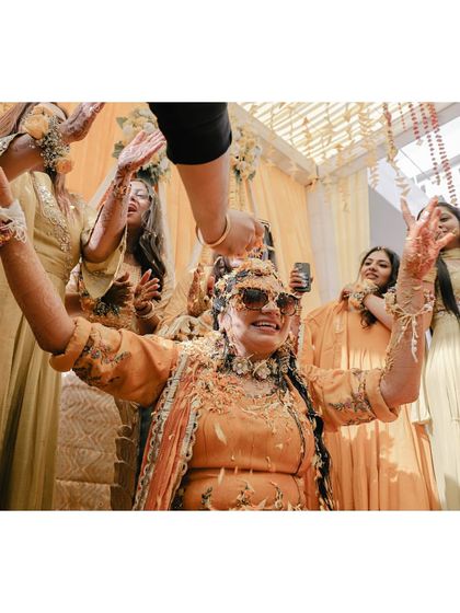 The bride, wearing sunglasses, enjoys being showered with petals during her fun-filled haldi.