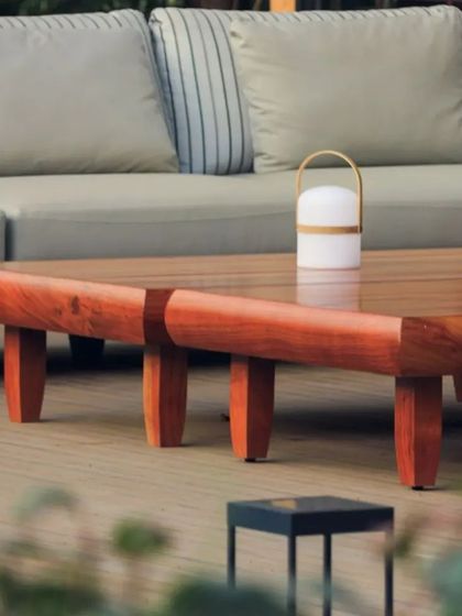 A close-up of the custom outdoor coffee table, crafted from a solid piece of wood. The furniture is both durable and sculptural, adding to the earthy, minimalist setting.