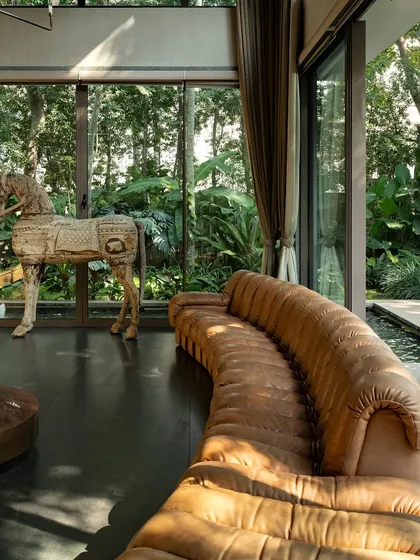 A close-up of a living area where a wooden horse sculpture stands before a glass wall, with the lush garden and pond visible just beyond. This layering of art, architecture, and nature creates a rich, multi-dimensional experience.