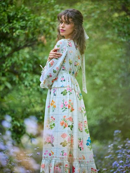A shot from a creative campaign for Pozruh, set in a lush, floral environment. The styling of this printed maxi dress is soft and romantic, perfectly matching the "secret garden" theme.