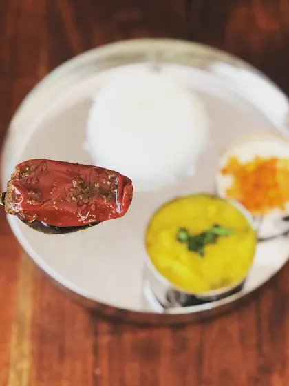 A single piece of my Bharwa Mirchi served on a spoon over a traditional thali. You can see the rich red colour and the spices it's packed with. It’s a true treat for spice lovers.