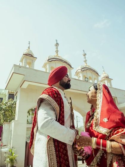 A low-angle shot of a Sikh couple standing outside the Gurudwara on their wedding day.