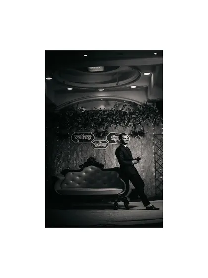 A stylish black and white portrait of the groom at his reception. He leans against a vintage-style sofa, creating a cool and classic photograph.