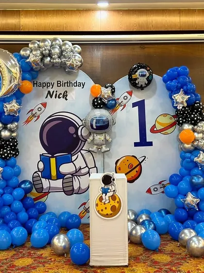 An out-of-this-world astronaut theme for a first birthday party. This backdrop features a custom printed banner, organic balloon garlands in blue, silver, and black, and themed foil balloons like a moon and astronaut.