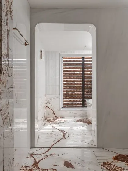 A view through an arched doorway into the master bathroom, showcasing the stunning white marble with dramatic red veining that clads the walls and floor.
