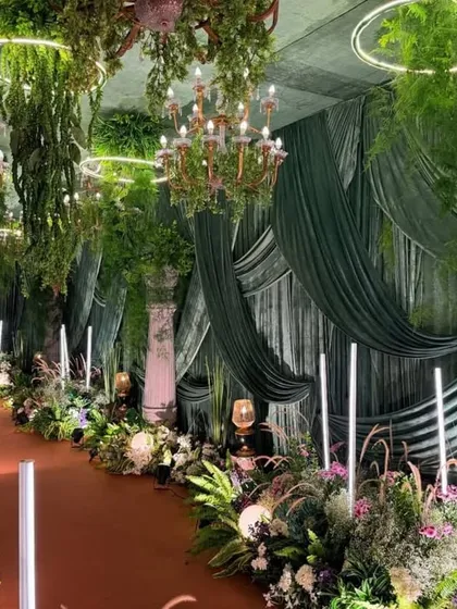 Imagine a sangeet night in an enchanted forest. This design uses deep green velvet drapes, dramatic chandeliers, and lush greenery to create a sophisticated and magical atmosphere perfect for a night of celebration.