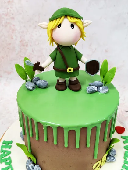 This Legend of Zelda cake features a detailed fondant figure of Link, the hero of Hyrule, standing on a green drip cake.
