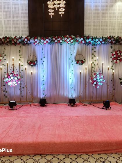This stage design for a wedding event uses a combination of white drapes, hanging floral baskets, and blue uplighting for a cool, elegant effect. The setup is perfect for an indoor banquet hall and provides a beautiful backdrop for photos.