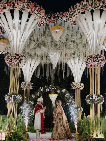 A breathtaking Varmala ceremony during a grand reception. The mandap is adorned with massive floral structures and cold pyro sparklers, creating a truly spectacular and memorable moment.